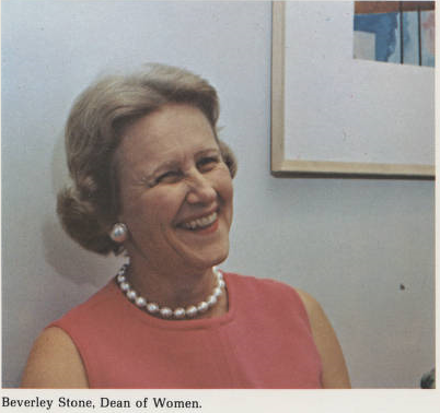 Potrait photograph of middle-aged woman. Colour photo. Smiling, not looking directly at camera. Wearing red/pink sleeveless top or dress and pearls. 