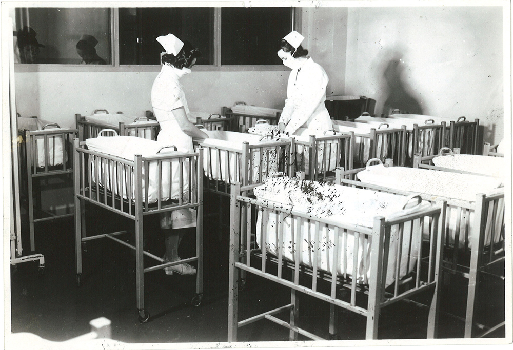 Interior shot of nursery, two nurses in masks tending to babies, Jewish General Hospital, Montreal. Courtesy of the Jewish Public Library Archives of Montreal. 