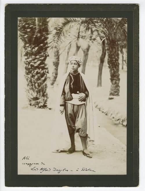 A boy poses standing in front of several palm trees.
