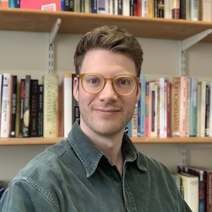 Tom Hulme seated in front of of bookshelves